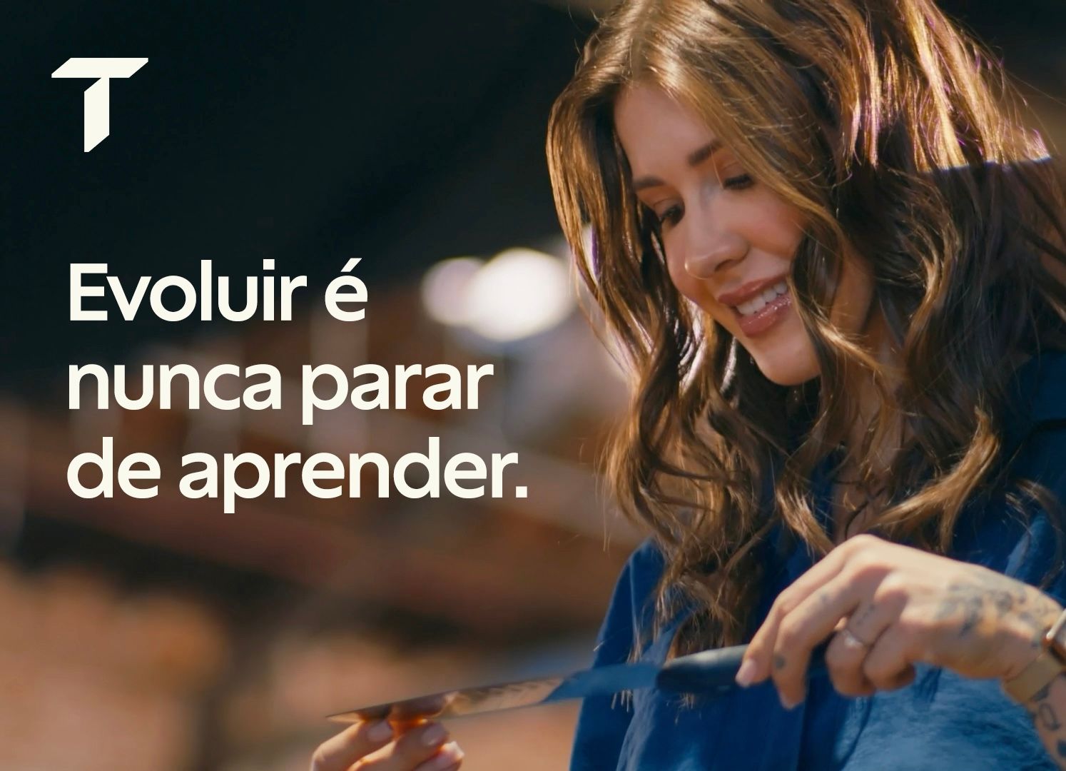 Fotografia de uma mulher jovem (Dani Choma) sorridente com cabelos castanhos ondulados, segurando e observando atentamente uma faca de chef. No canto esquerdo, há um logo em formato de "T" e a frase em destaque: "Evoluir é nunca parar de aprender." A imag