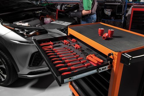 Visão geral de oficina automotiva equipada com armários modulares, bancadas de trabalho e carros de ferramentas Tramontina PRO nas cores laranja e preta.
