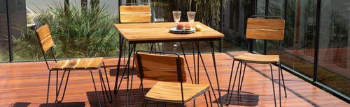 Conjunto de varanda Tramontina com mesa quadrada e quatro cadeiras de madeira teca e pés metálicos pretos sobre deck de madeira.