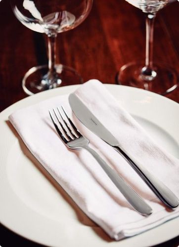 Table set with wine glasses, plate and napkin with flatware on it.