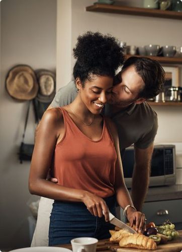 Black woman cutting bread with a Tramontina knife, while a white man kisses her face.