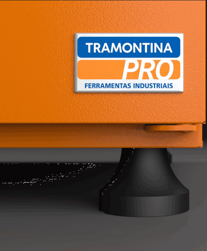 Close-up do logo retangular "TRAMONTINA PRO FERRAMENTAS INDUSTRIAIS" em azul, laranja e branco, afixado em uma superfície laranja texturizada. Abaixo do logo, parte de um pé preto arredondado é visível.