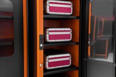 Armário industrial laranja e preto Tramontina PRO Smart System com porta aberta exibindo maletas de ferramentas organizadas em prateleiras internas.
