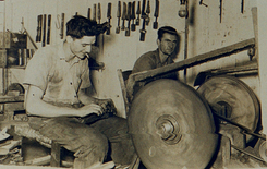Fotografia antiga de dois trabalhadores operando grandes mós de pedra para o polimento artesanal de lâminas em uma oficina.
