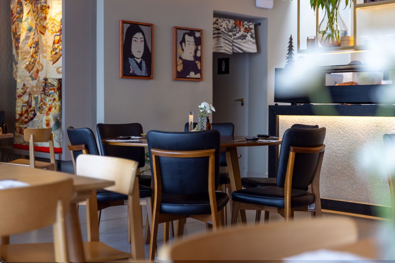 Salão de restaurante japonês com decoração oriental, apresentando mesa redonda com cadeiras estofadas em couro preto e estrutura de madeira Tramontina Hospitality.